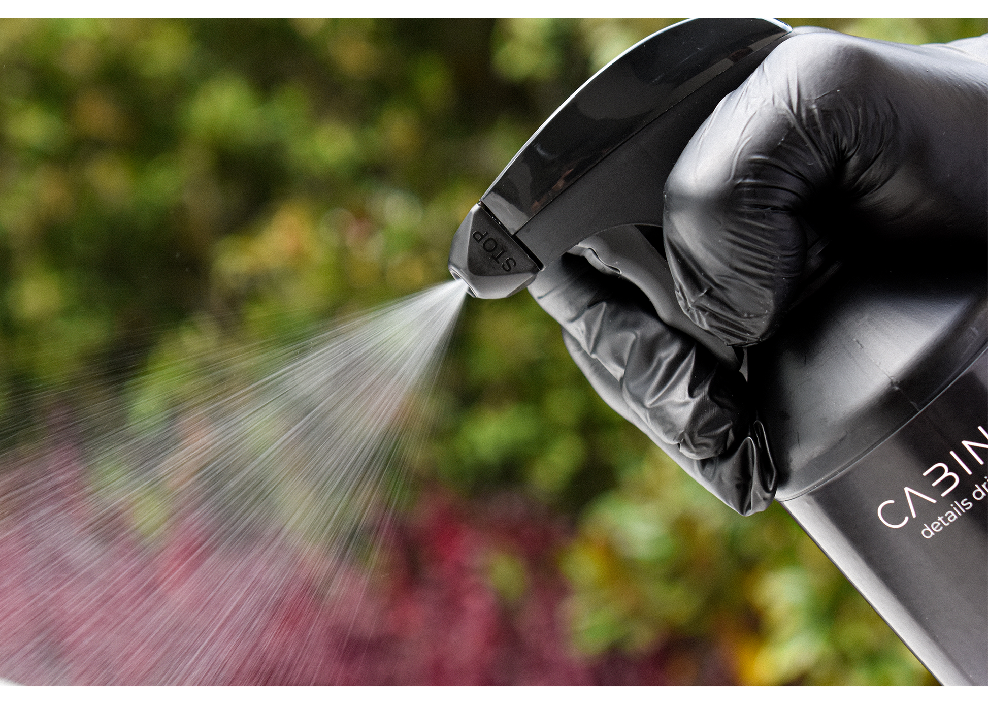 Hand wearing a black glove holding a CABIN8 spray bottle with water spraying outdoors.
